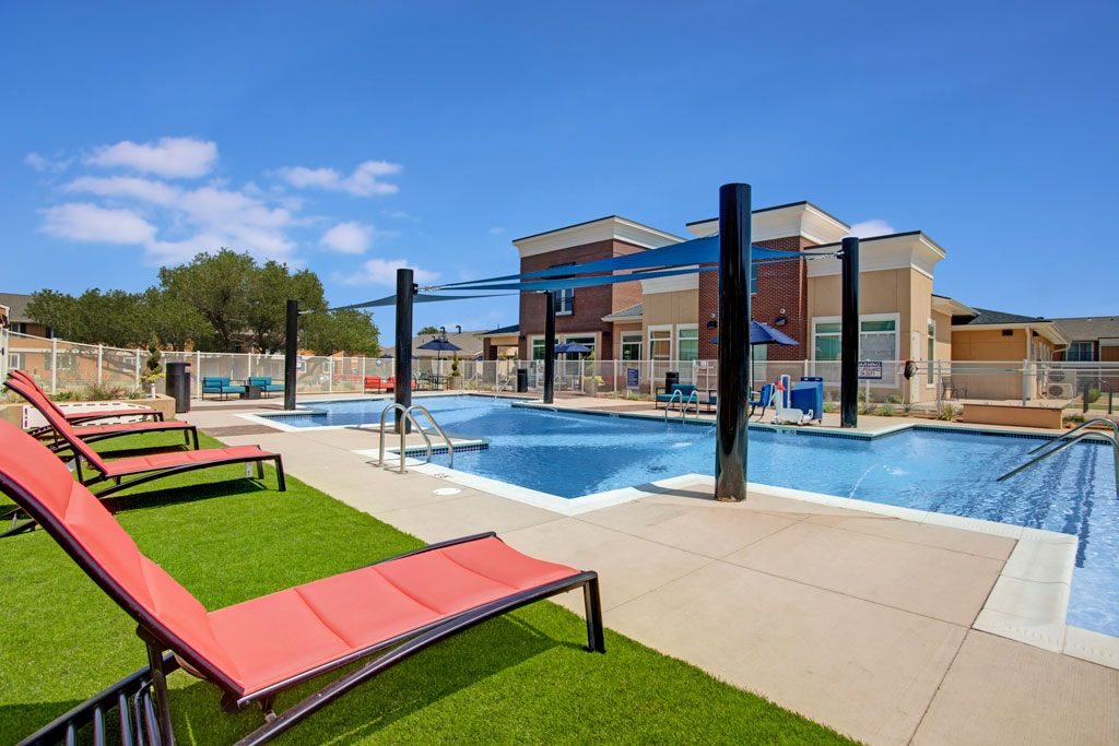 A pool with red sun loungers and a building in the background.
